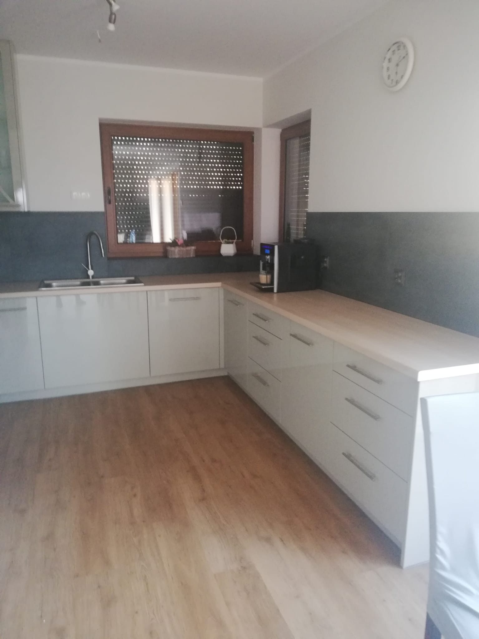 Jasna, nowoczesna kuchnia z drewnianymi roletami w oknie. Na blacie stoi ekspres do kawy. Ujęcie z poziomu podłogi, podkreślające przestrzeń.