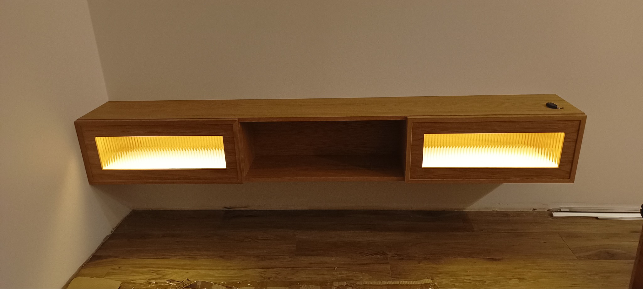 Drewniana szafka wisząca z oświetleniem LED, dębowa okleina, minimalistyczny design, ciepłe światło, widok z dołu, nowoczesne wnętrze.