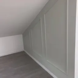 Ściana w pokoju na poddaszu z szarymi panelami dekoracyjnymi i szarą podłogą z paneli.