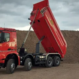 Czerwona wywrotka Mercedes Arocs z podniesioną skrzynią ładunkową na tle hałdy gruzu