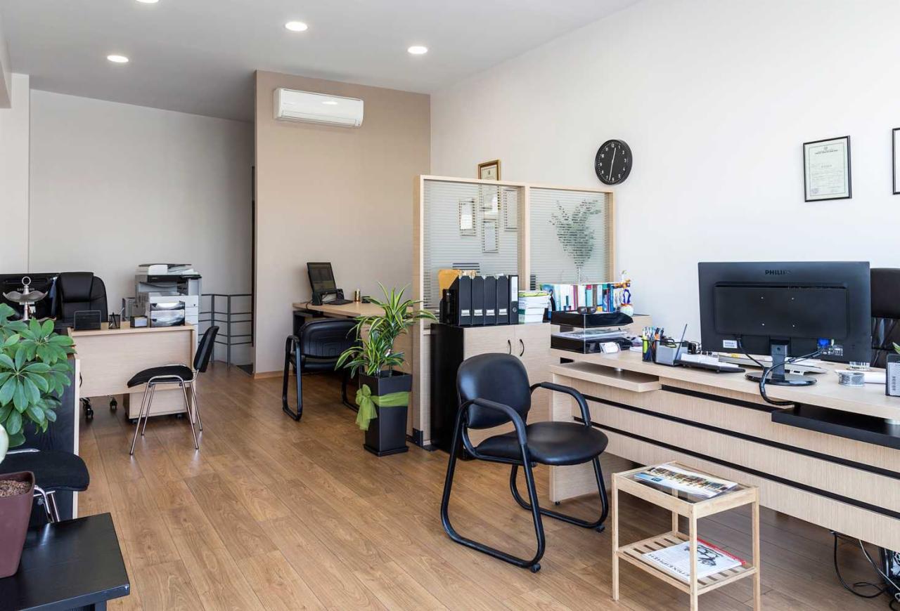 Jasne, przestronne wnętrze biura z drewnianą podłogą, biurkami, krzesłami, roślinami doniczkowymi i klimatyzatorem na ścianie.