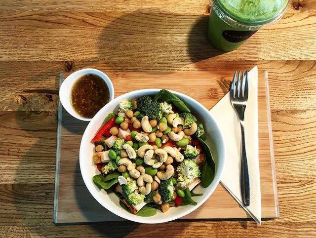 Zdrowa sałatka z brokułami, ciecierzycą, orzechami nerkowca i sosem na drewnianej desce obok zielonego smoothie i widelca.