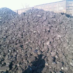 Dwa pryzmy węgla kamiennego o granulacji 50-200mm na placu składowym, z wagonami kolejowymi w tle, oświetlone jasnym światłem słonecznym.