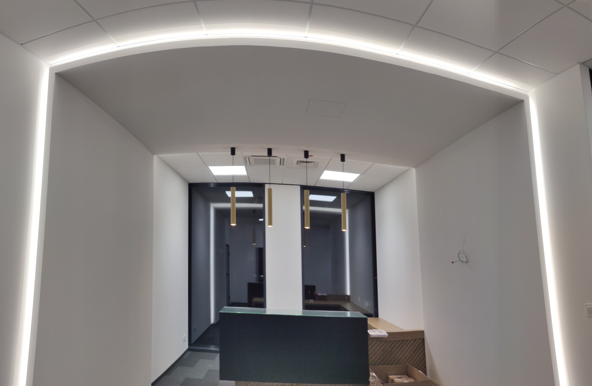 Nowoczesne biuro z podświetlanymi ścianami i sufitem, minimalistyczne lampy wiszące nad recepcją.