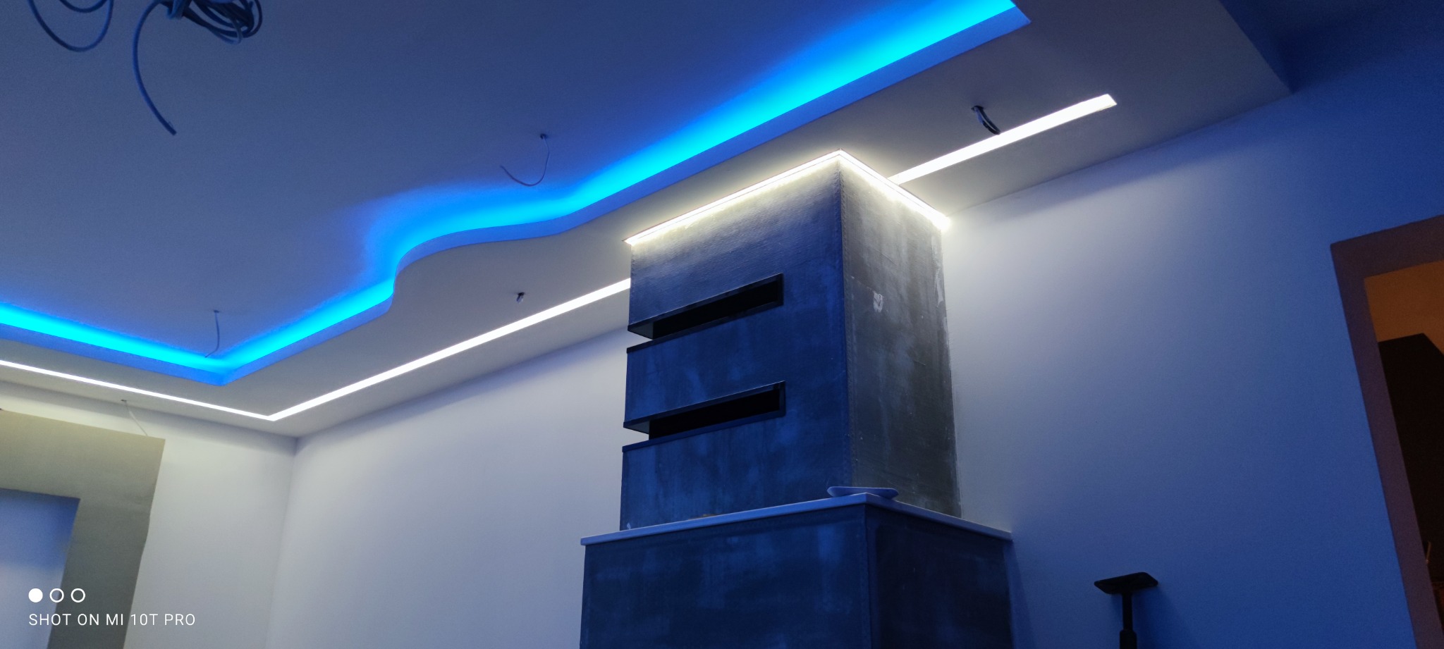 Nowoczesne oświetlenie sufitowe LED w kolorze białym i niebieskim, z elementami dekoracyjnymi i betonową konstrukcją architektoniczną w tle.