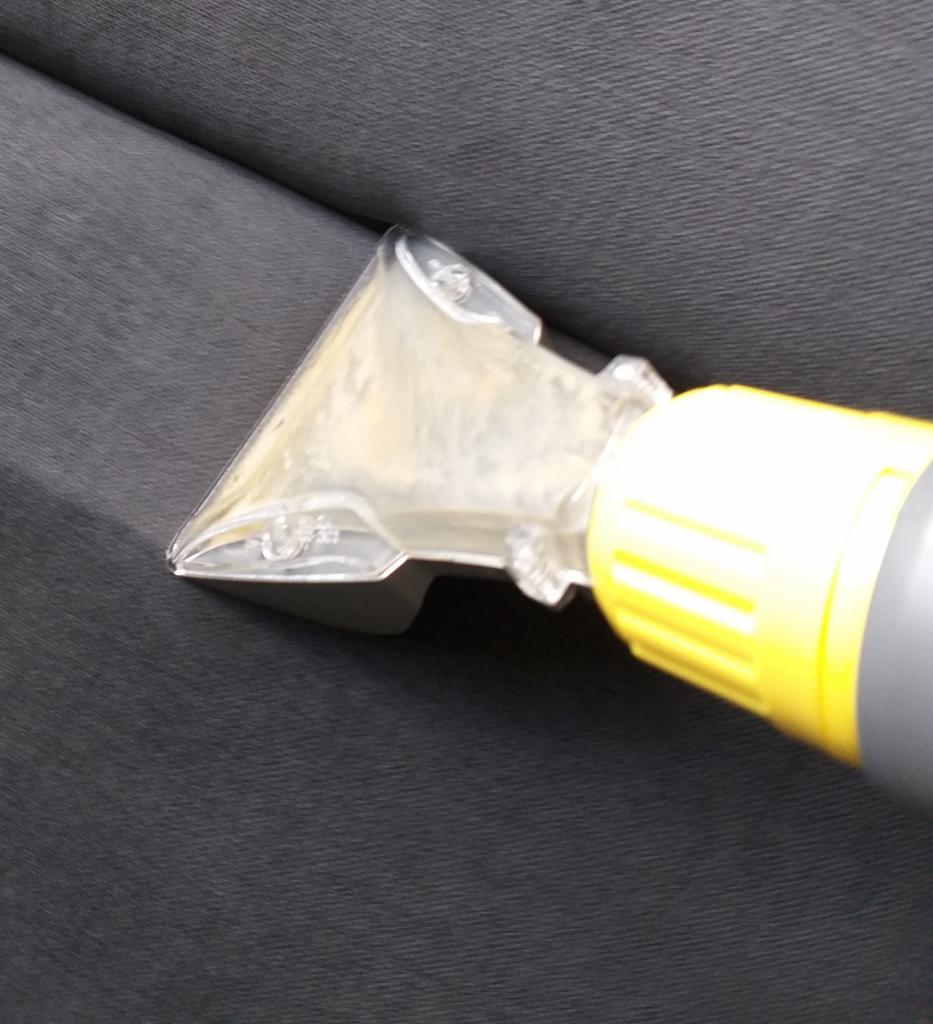 Dysza odkurzacza piorącego z żółtą obudową w trakcie czyszczenia ciemnoszarej tapicerki meblowej, widoczne ślady wilgoci.