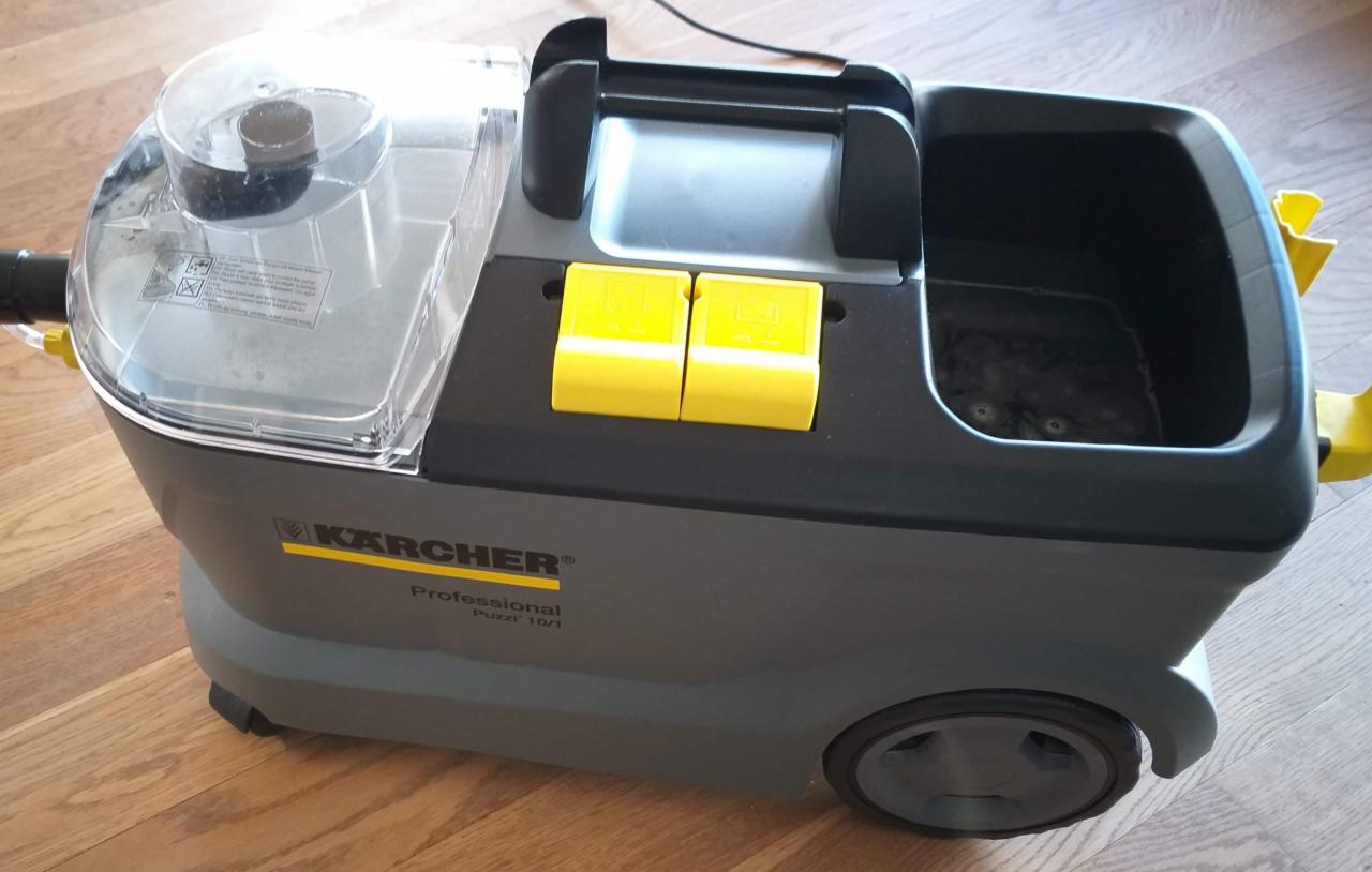 Profesjonalny odkurzacz piorący Kärcher Puzzi 10/1 na drewnianej podłodze, widoczne żółte elementy i przezroczysty zbiornik na wodę.