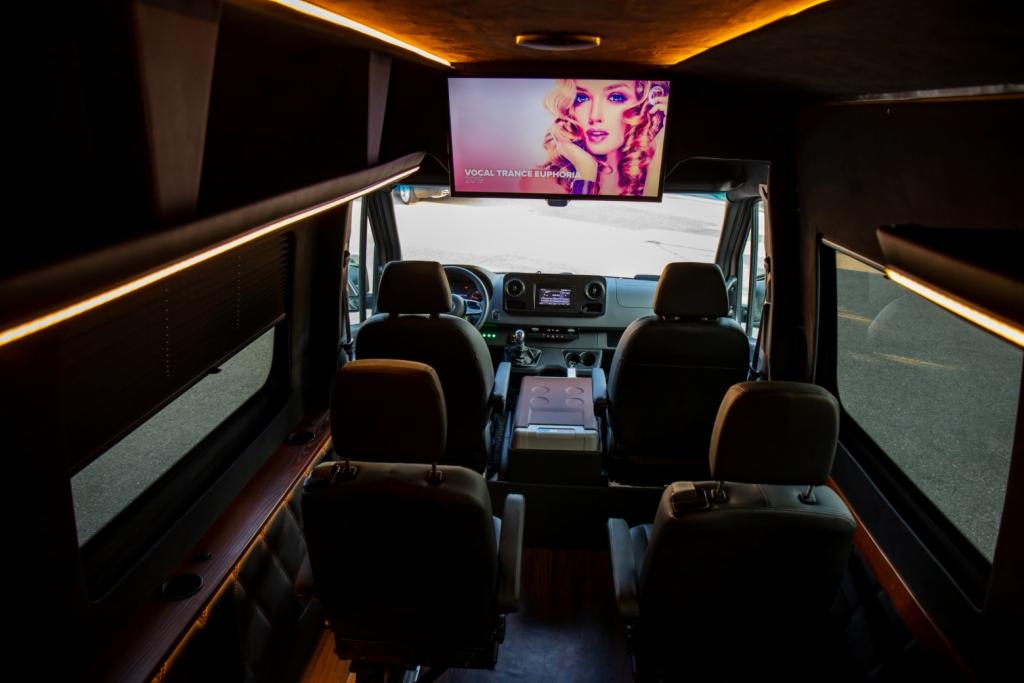 Wnętrze luksusowego vana z skórzanymi siedzeniami, oświetleniem LED i telewizorem wyświetlającym teledysk z gatunku Vocal Trance Euphoria.