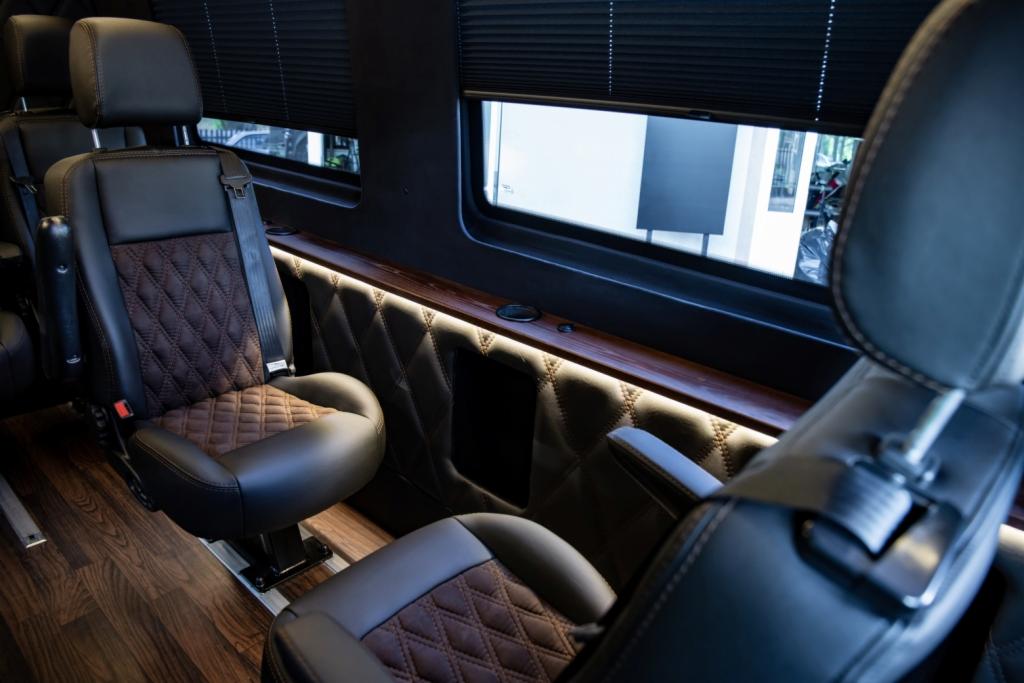 Wnętrze luksusowego busa z brązowo-czarnymi skórzanymi fotelami w romby, oświetleniem LED i drewnianą podłogą.