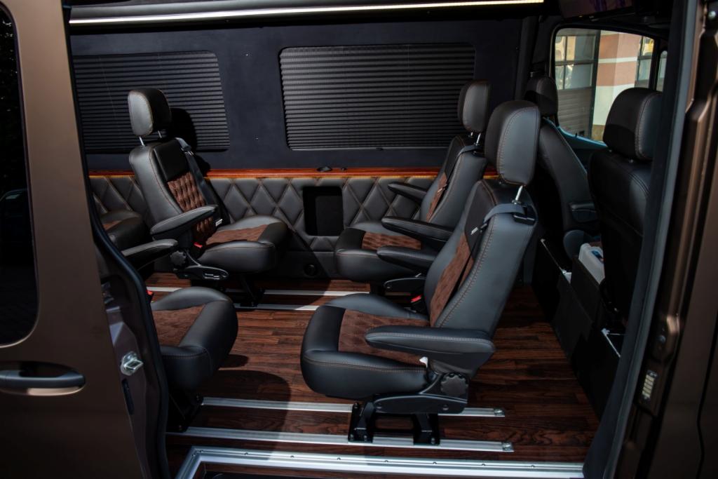 Wnętrze luksusowego vana z czarnymi skórzanymi fotelami z brązowymi wstawkami, drewnianą podłogą i pikowaną tapicerką ścian.