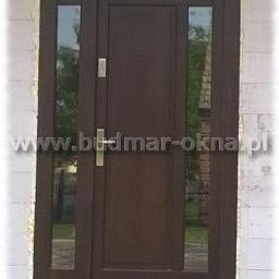 BUDMAR Producent okien i drzwi z drewna - Brązowe drzwi wejściowe z dwoma bocznymi przeszkleniami, widoczny zamek i klamka, zamontowane w surowym murze z betonu komórkowego, z widocznym adresem strony internetowej na zdjęciu.