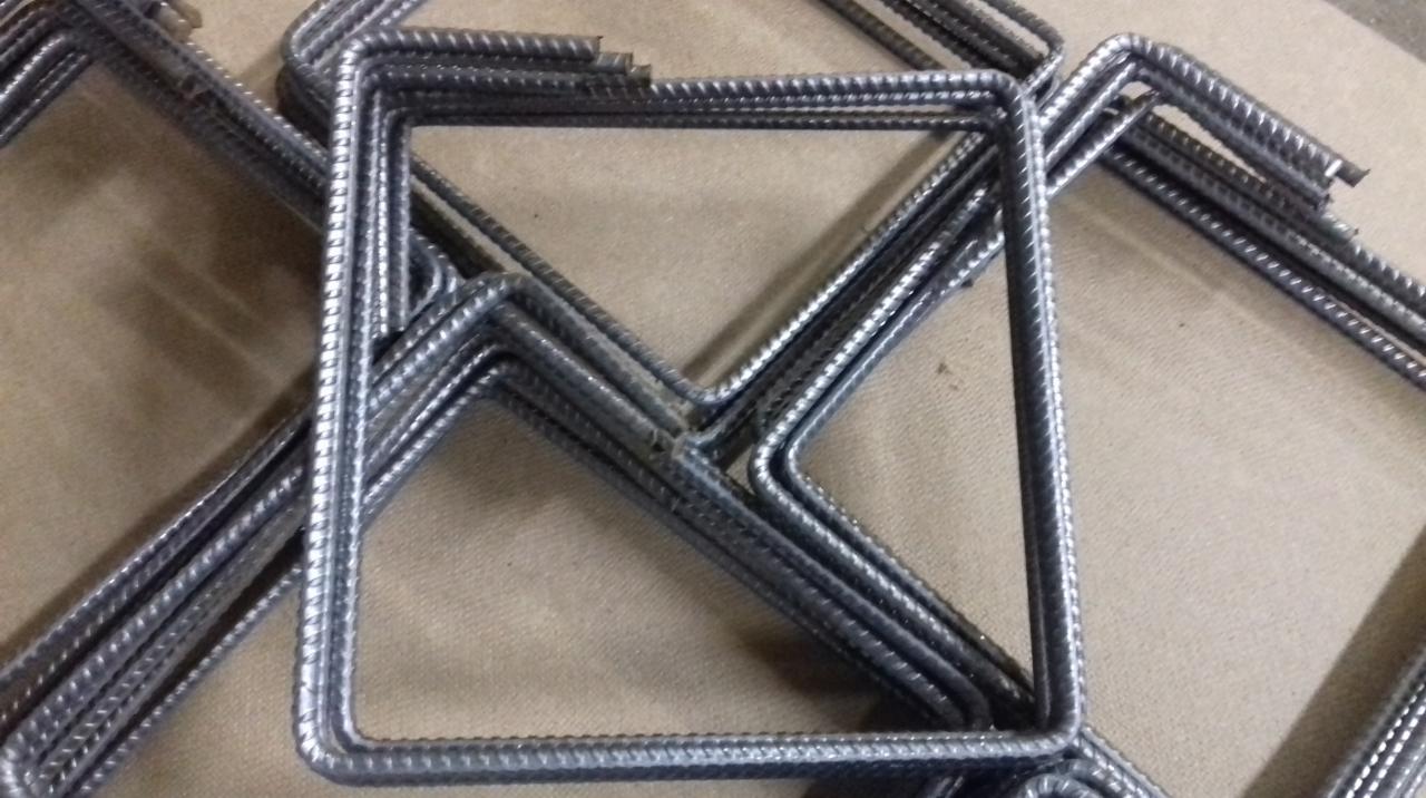 Kwadratowe strzemiona z żebrowanej stali ułożone warstwami na płaskiej powierzchni.
