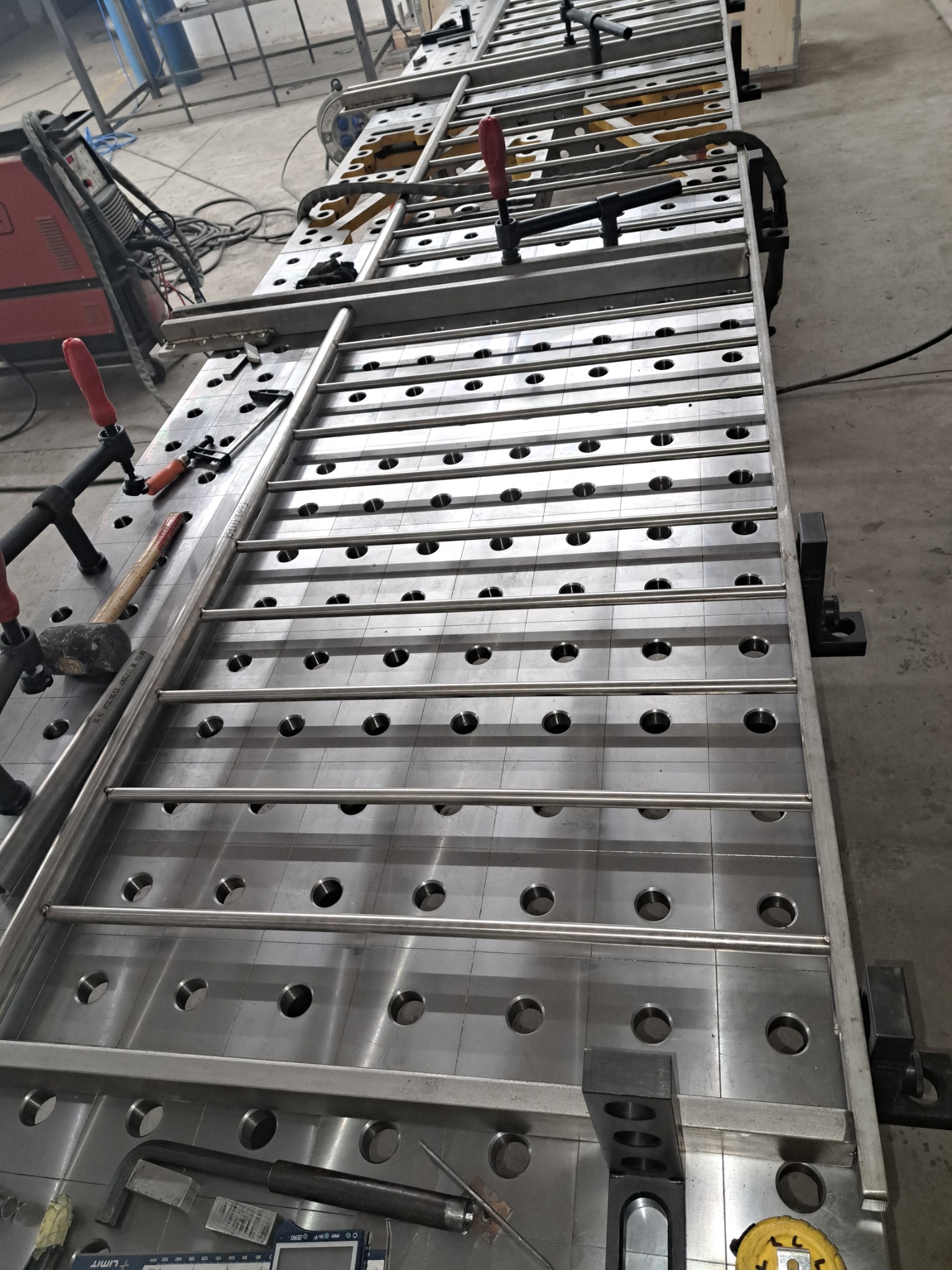 Stół spawalniczy z zamontowanymi elementami konstrukcji stalowej, narzędzia i zaciski widoczne na blacie. Widok z góry.