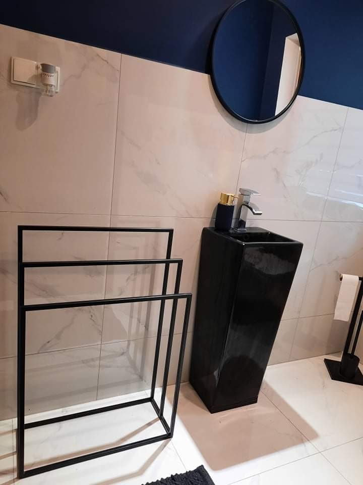 Nowoczesna łazienka z czarną umywalką na postumencie, okrągłym lustrem i minimalistycznym wieszakiem na ręczniki. Marmurowe płytki i granatowy sufit.