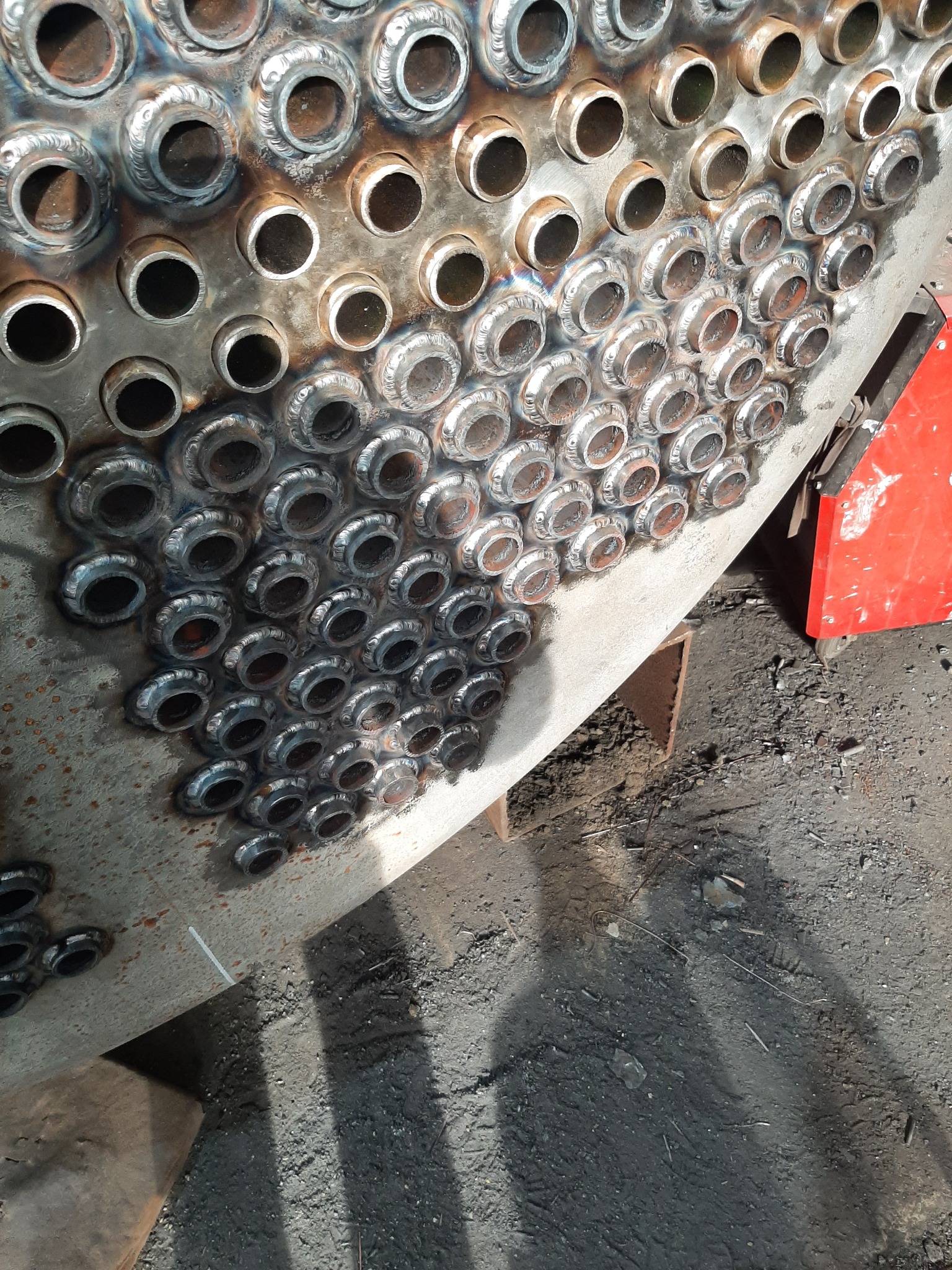 Spoina na metalowej konstrukcji z licznymi otworami, widoczne ślady spawania i metaliczne wykończenie. Częściowo zakończony proces łączenia elementów.