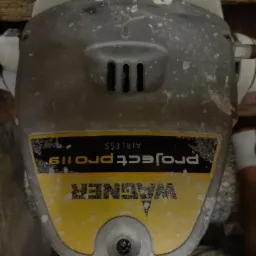 Używany agregat malarski Wagner Project Pro 119 z widocznymi śladami farby, ustawiony na podłodze w trakcie remontu mieszkania.