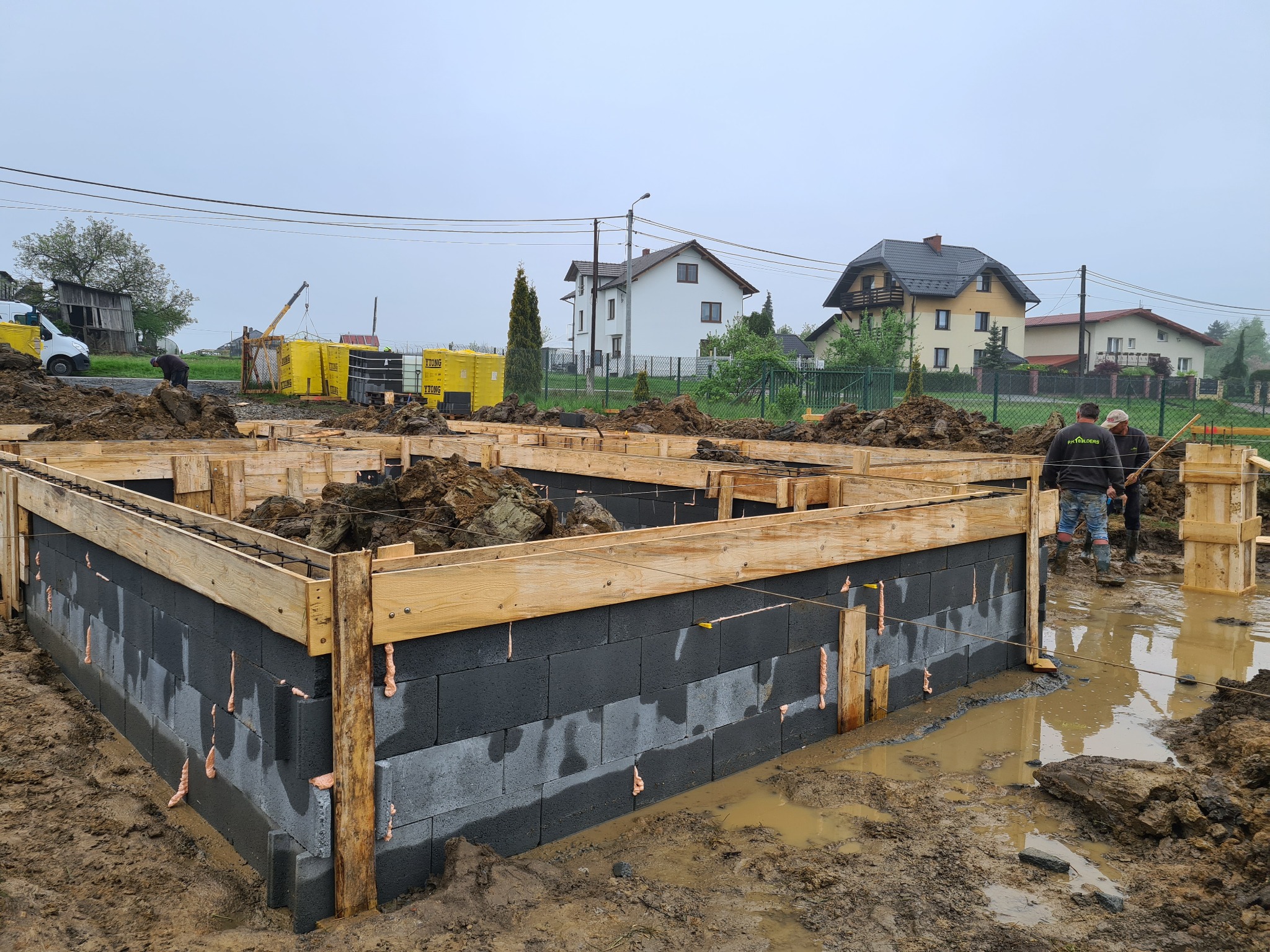 Fundamenty z bloczków betonowych, wzmocnione drewnianą konstrukcją szalunkową, w trakcie budowy domu jednorodzinnego, widoczne ślady pianki montażowej i błoto.