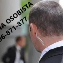 Ochroniarz z widocznym zestawem słuchawkowym, w tle rozmyta sylwetka innej osoby, na zdjęciu widoczny napis 'Ochrona osobista, tel. 796-871-877'.