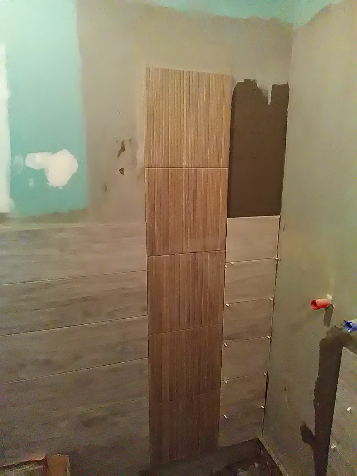 Montaż pionowego panelu z płytek imitujących drewno na ścianie w łazience, widoczne krzyżyki dystansowe i ślady zaprawy.