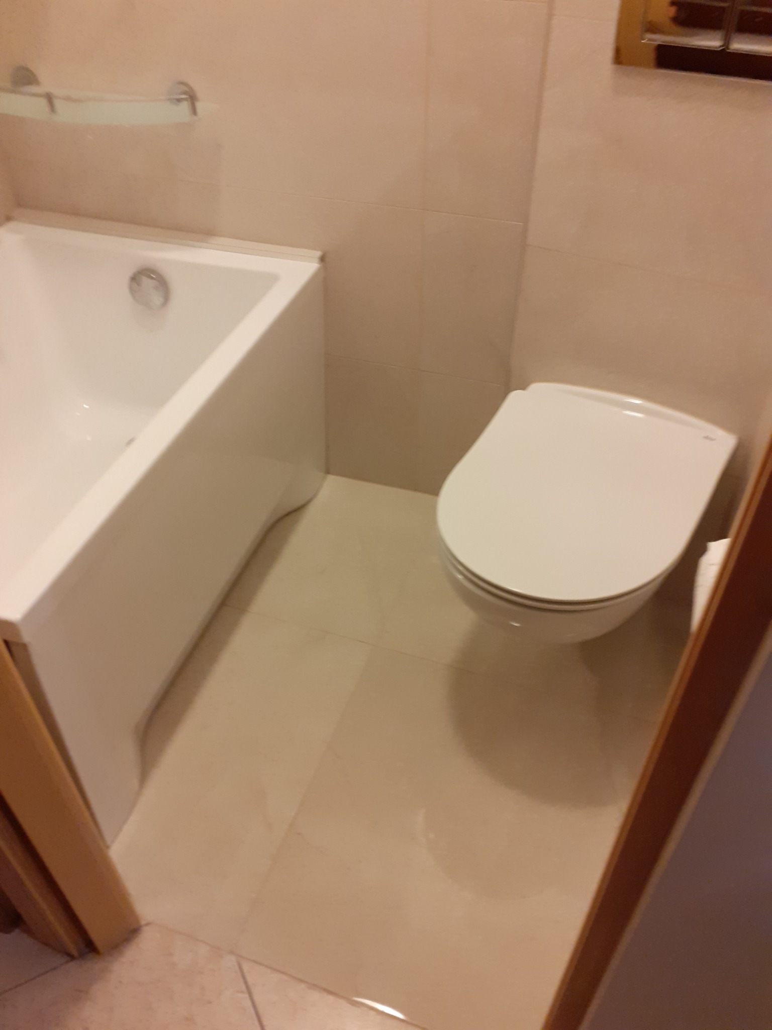 Jasna łazienka z białą wanną i wiszącą toaletą, wykończona beżowymi płytkami.