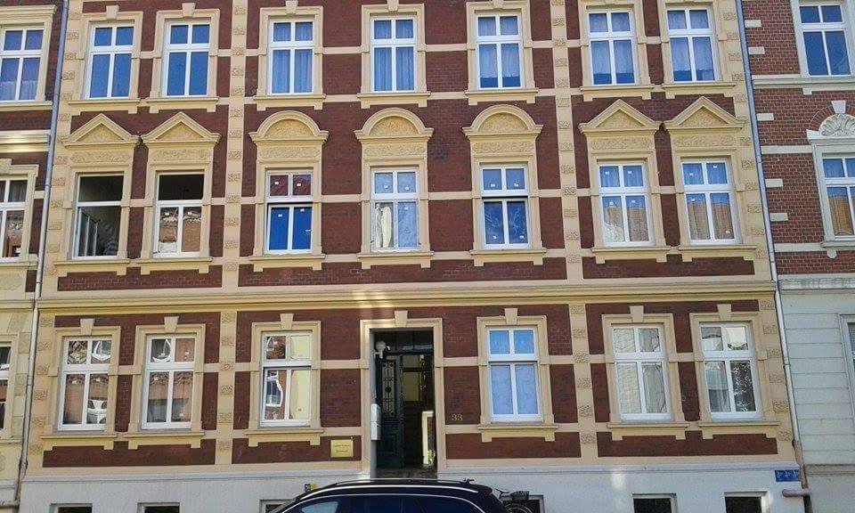 Fasada kamienicy z licznymi oknami z białymi ramami, niektóre z dekoracyjnymi obramowaniami, widok z dołu na elewację budynku.