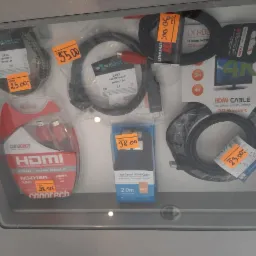 Różne kable HDMI w opakowaniach i bez, z cenami, ułożone na półce w sklepie, widoczne marki Conotech, Opticum i Master.