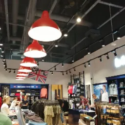 Wnętrze sklepu odzieżowego z oświetleniem szynowym i czerwonymi lampami wiszącymi, widoczny fragment flagi brytyjskiej jako element dekoracyjny.