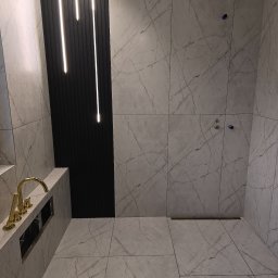 Kornbud - Wykończona łazienka z marmurowymi płytkami, złotą armaturą i podświetlanym panelem ściennym.