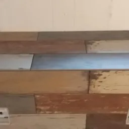 Ułożona podłoga z paneli imitujących postarzane drewno w odcieniach szarości, beżu i brązu, widoczne dwa gniazdka elektryczne w podłodze.