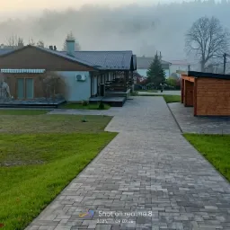 Szeroki, szary chodnik z kostki brukowej prowadzi do domu z muralem wilka na ścianie, widok w mglisty poranek.