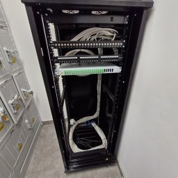 SMART INSTAL - Szafa rackowa z patch panelem i uporządkowanymi kablami sieciowymi, widoczne numery portów, obok szafy elektryczne z ostrzeżeniami o wysokim napięciu.