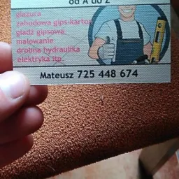 Dłoń trzyma wizytówkę z ofertą usług remontowo-wykończeniowych od A do Z, z ilustracją majstra i numerem telefonu.