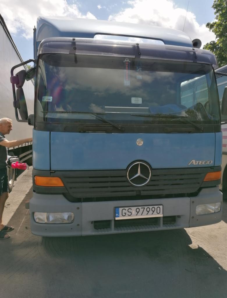 Błękitny samochód ciężarowy Mercedes Atego z widoczną tablicą rejestracyjną GS 97990, myty przez mężczyznę w krótkich spodenkach.