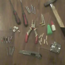 Zestaw narzędzi i akcesoriów na drewnianej powierzchni: młotek, śrubokręty, kombinerki, miara zwijana, nożyk, kołki, śruby, gwoździe oraz klej.