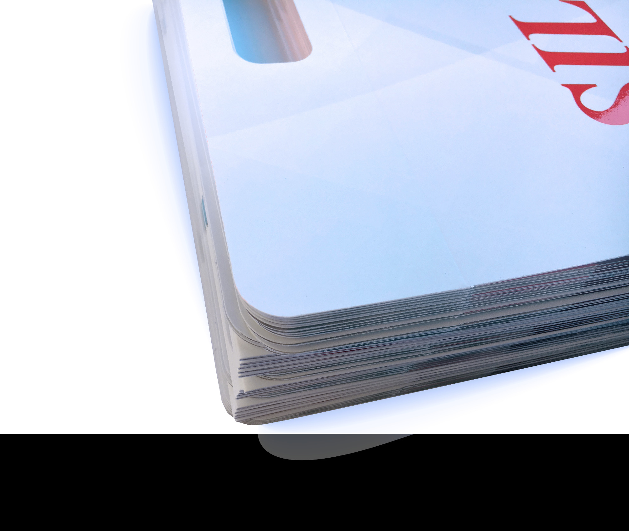 Stos zadrukowanych arkuszy papieru z widocznym fragmentem czerwonego napisu na górnym arkuszu, ułożony pod kątem, z widocznymi krawędziami i warstwami papieru.