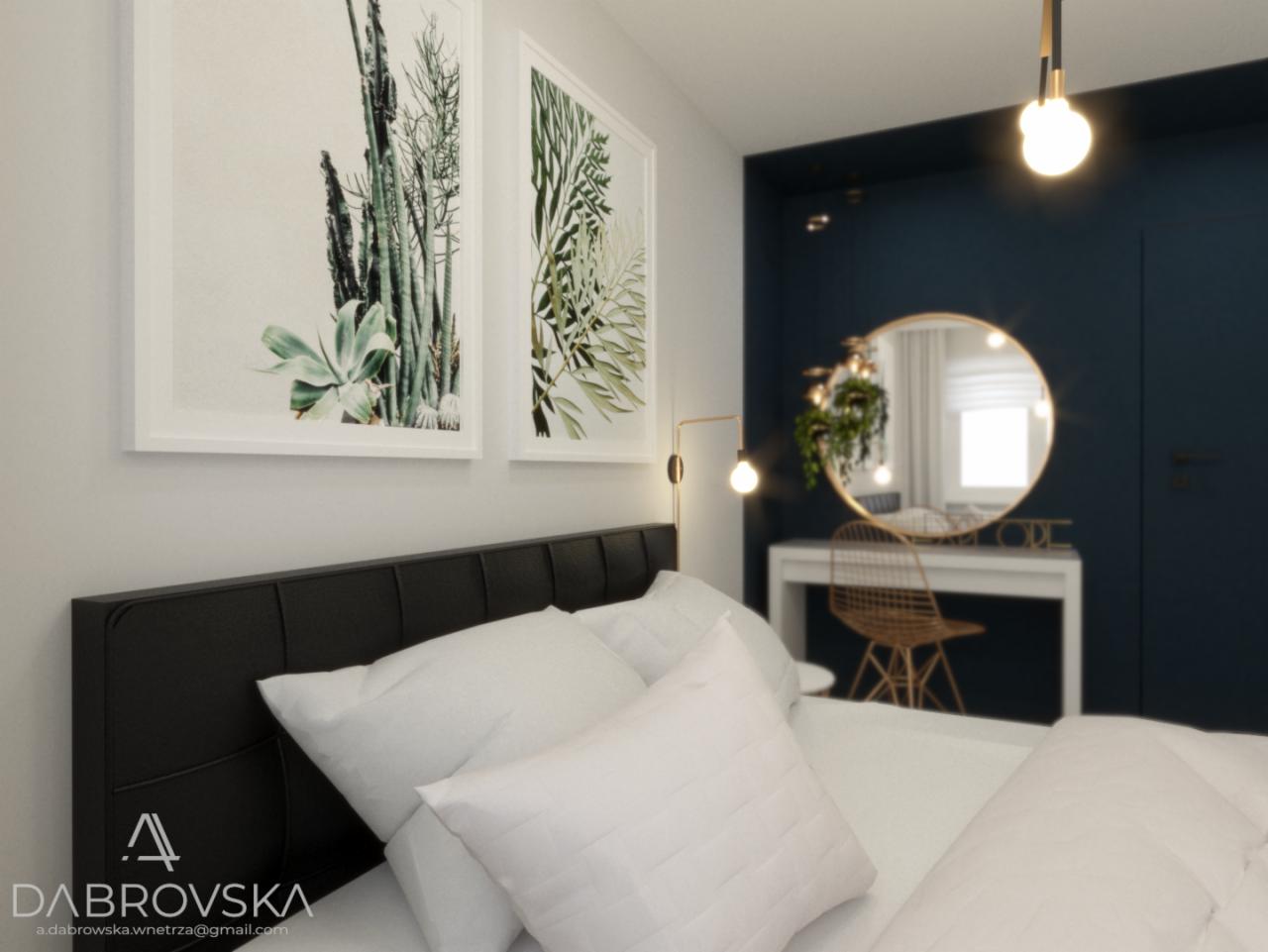 Nowoczesna sypialnia z czarnym wezgłowiem łóżka, białymi poduszkami, dekoracyjnymi obrazami z motywami roślinnymi, toaletką z okrągłym lustrem w złotej ramie i złotym krzesłem, oświetlona wiszącą...