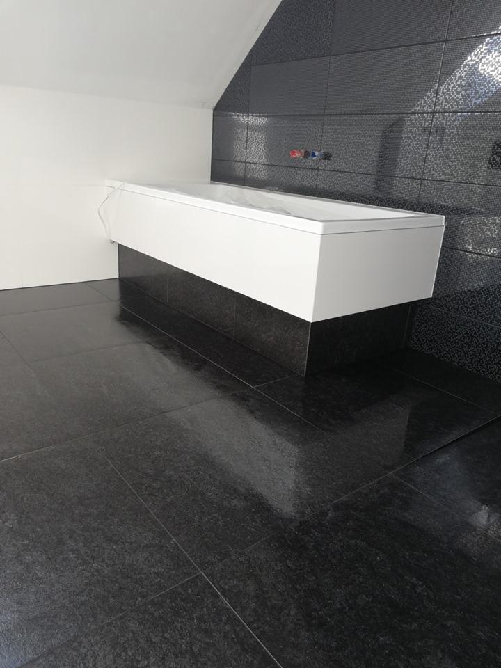 Nowoczesna łazienka w Bukowie z czarną, błyszczącą podłogą z płytek i ścianą z dekoracyjnych płytek za białą wanną.