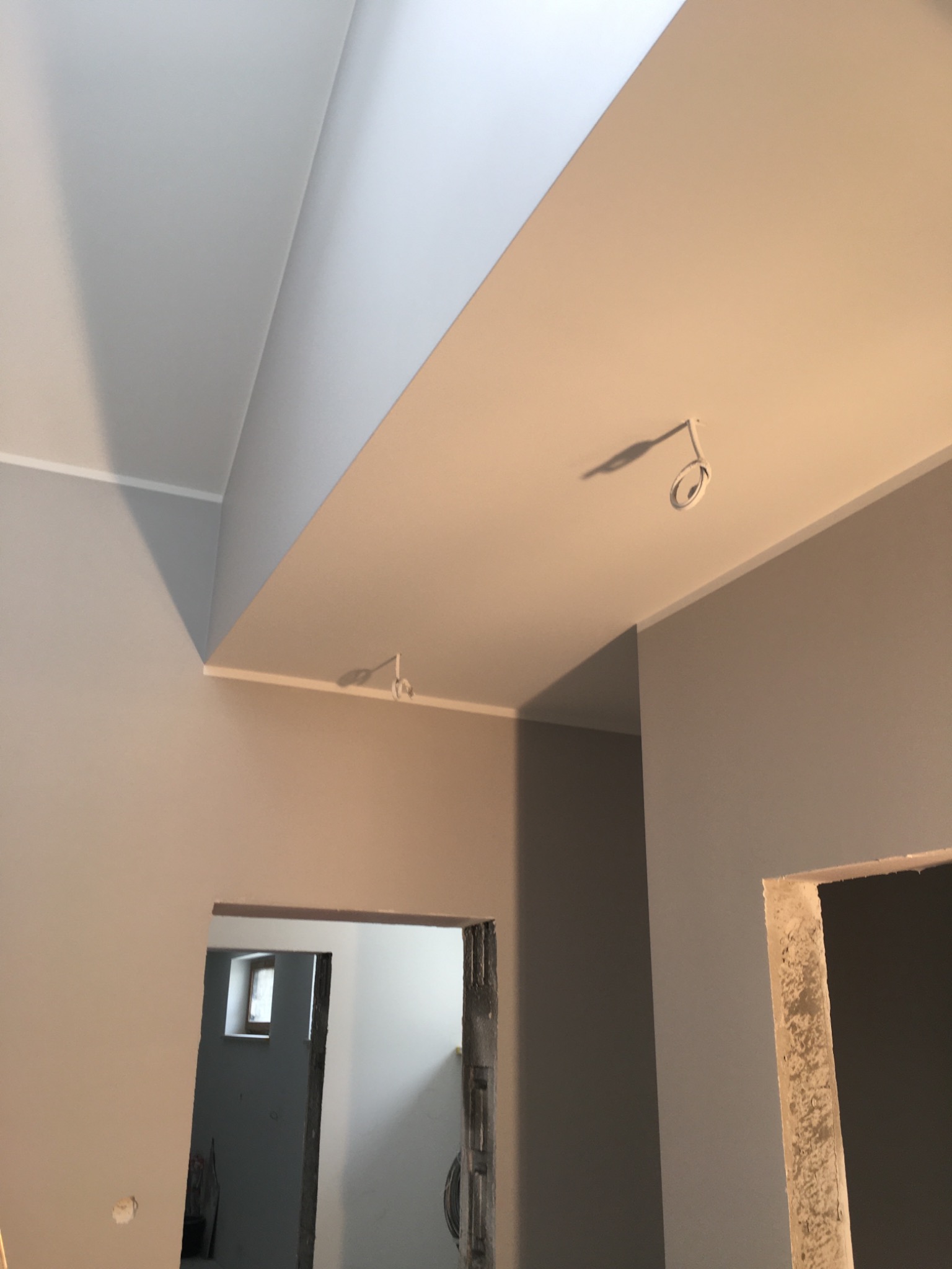 Świeżo pomalowane wnętrze w odcieniach szarości i bieli, widoczne surowe otwory drzwiowe i wystające kable oświetleniowe.