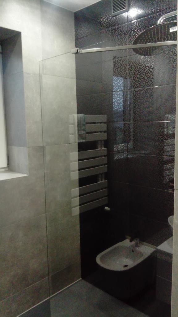 Nowoczesna łazienka z szarymi i czarnymi płytkami, szklaną kabiną prysznicową, grzejnikiem drabinkowym i bidetem.