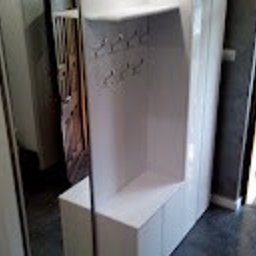 Meblesystem - Biała szafa wnękowa z lustrem i wieszakami, widok z boku, oświetlenie dzienne, minimalistyczny design, szara ściana w tle.