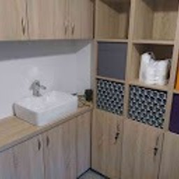 Meblesystem - Jasna zabudowa łazienkowa z umywalką nablatową i szafkami z półkami. Uwagę zwracają kolorowe pojemniki w otwartych półkach i minimalistyczna bateria.