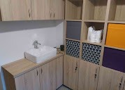 Jasna zabudowa łazienkowa z umywalką nablatową i szafkami z półkami. Uwagę zwracają kolorowe pojemniki w otwartych półkach i minimalistyczna bateria.