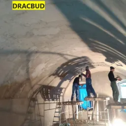 Trzech robotników na rusztowaniach aplikuje tynk na sklepieniu łukowym, widoczne cienie narzędzi i sylwetek na ścianie, logo firmy w lewym górnym rogu.