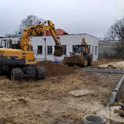 Dwie żółte koparki Liebherr pracują na placu budowy, przygotowując teren pod fundamenty nowego budynku w pochmurny dzień.