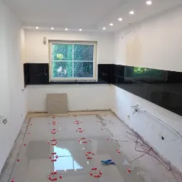 Kładzenie jasnych płytek podłogowych w kuchni z czarnymi płytkami na ścianie, widoczne krzyżyki dystansowe i poziomica.