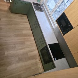 Rawel-Instal - Nowoczesna kuchnia w odcieniach zieleni i drewna z blatem imitującym beton, z widoczną płytą indukcyjną i piekarnikiem. Ujęcie z góry, prezentujące układ i wykończenie.