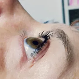 Detal widoku oka z bliska po zabiegu przedłużania rzęs, widoczne pojedyncze sztuczne rzęsy, naturalne brwi i delikatne zmarszczki w kąciku oka.