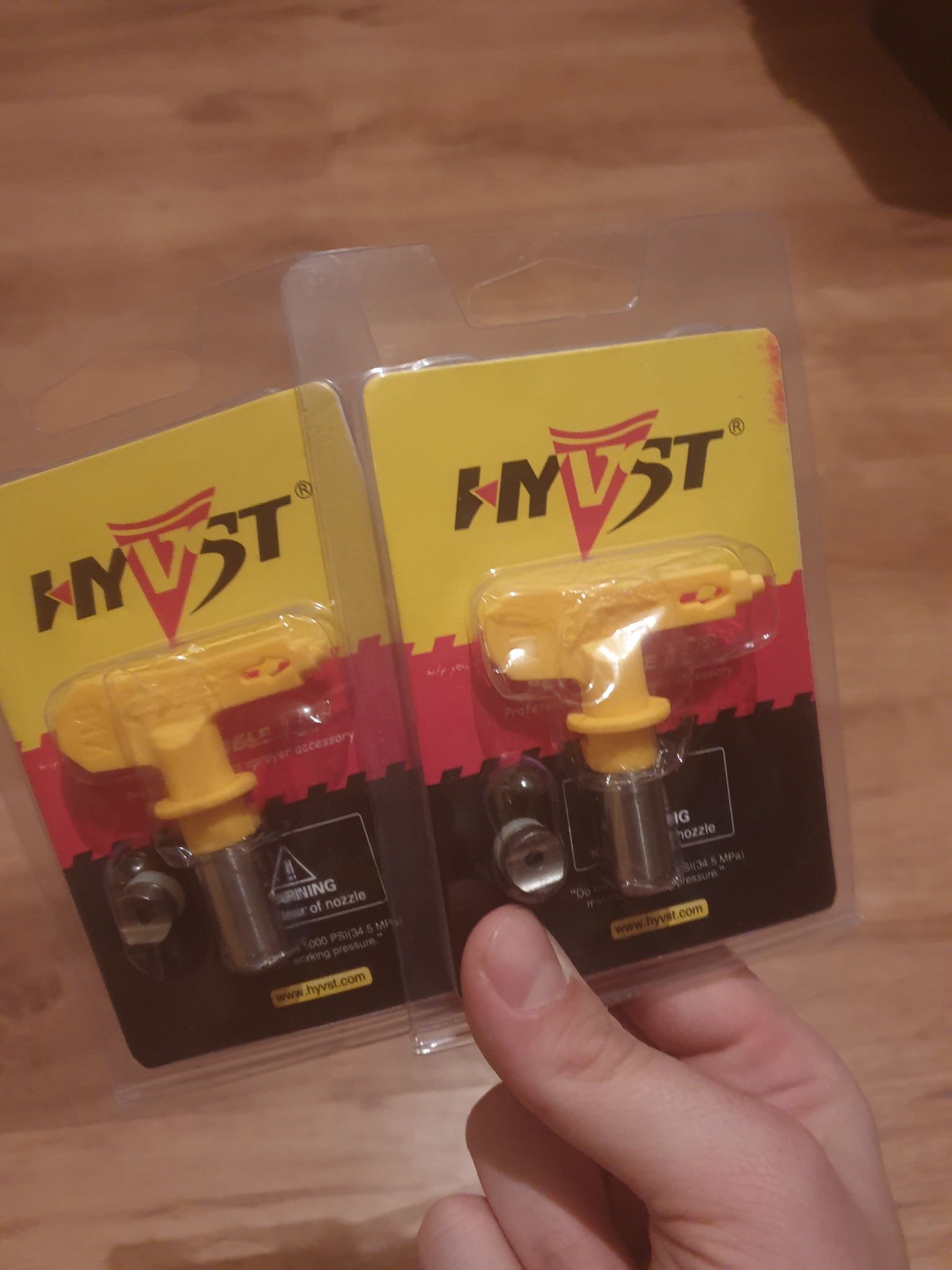 Dwie dysze natryskowe HVST w żółtych obudowach na tle drewnianej powierzchni, trzymane w dłoni.