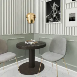 Stylowe wnętrze z okrągłym stolikiem, dwoma szarymi krzesłami na złotych nogach, wiszącą złotą lampą i czarno-białymi obrazami na ścianie w pionowe pasy.