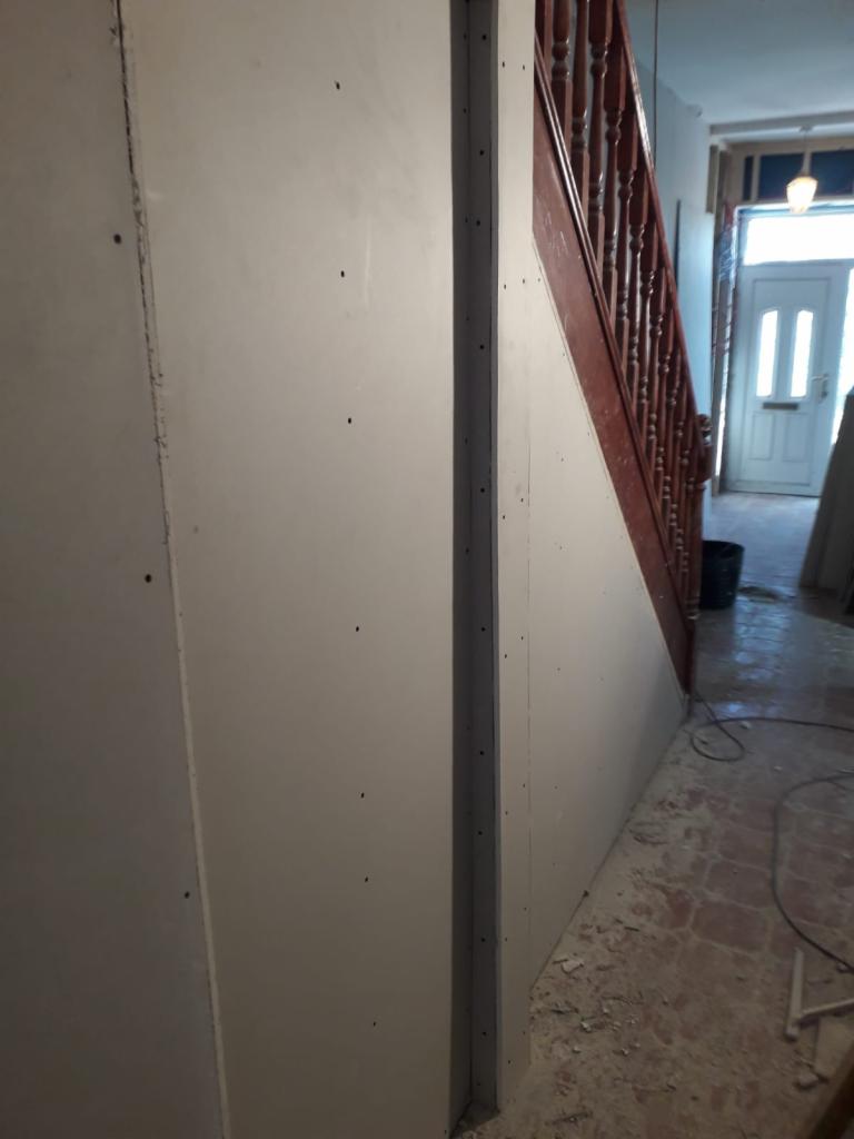 Montaż płyt gipsowo-kartonowych na ścianie klatki schodowej, widoczne ślady po szpachlowaniu, przygotowanie do dalszych prac wykończeniowych.